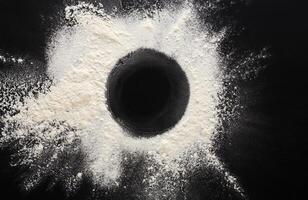 Abstract background. Sprinkled wheat flour circle, round spot on black. Top view on blackboard. Baking concept, cooking dough or pastry. photo