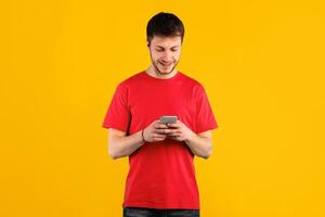 Amazing Application. Portrait of happy smiling young man using smartphone standing isolated over blue studio background, copy space. Guy chatting online, typing sms, browsing social media photo