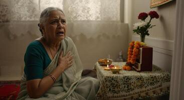 Elderly indian woman in traditional attire praying in a devotional home setting photo