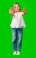 Young girl with long hair raises hand in a stop gesture against a green background photo