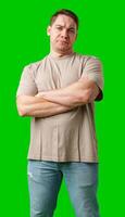 Young man making a disgusted expression while standing against a bright green background photo