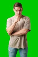 A young man with a serious expression pointing towards the viewer, standing against a bright green background photo