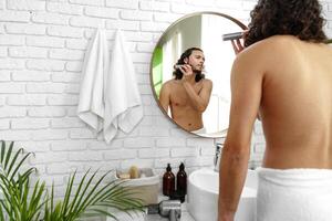 A man with curly hair grooming himself in the bathroom while looking into a round mirror photo