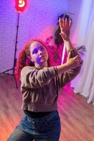 A young woman with red hair dances in a studio lit by pink and purple lights photo