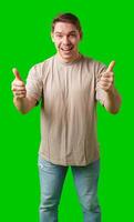 A man in a beige shirt gives a thumbs up while standing against a green background photo