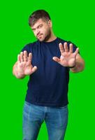 A man with a serious expression holds up both hands in a stopping gesture against a bright green background photo