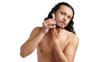 A man with curly hair grooming his beard in a well-lit space while using a straight razor photo