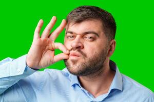 A man makes a funny face while forming an OK gesture with his hand against a bright green background photo