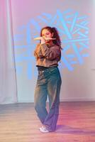A young woman strikes a pose during a dance practice session in a studio with colorful lights photo