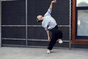A dancer performs a move in front of a chain-link fence on a city street photo