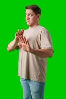 A man with a neutral expression gestures defensively against a bright green background photo