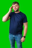A man with closed eyes holds his head in a thoughtful pose against a bright green backdrop photo