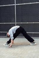 A person stretches in front of a chain link fence, reaching their hands down to touch the pavement photo