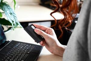 The credit card is being held in the right hand, with the left hand on a laptop keyboard. photo
