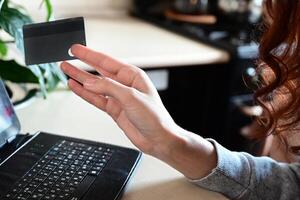 An overhead shot of a person's right hand holding a black credit card, with the left hand on a laptop keyboard. photo