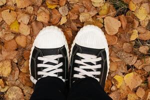 Legs of a teenager in boots made of textile material, standing on the ground with fallen leaves photo