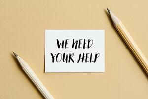 We need your help message written on a white card with pencil. Conceptual we need your help symbol. Copy space. photo