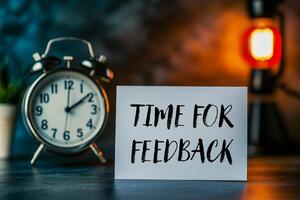 Time for feedback message written on a white card with a clock in the background photo