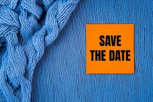 Save the date message written on orange card on blue fabric background. Conceptual save the date symbol. Copy space. photo