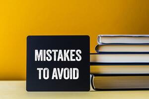 Mistakes to avoid message written on black card with stack of books. Conceptual mistakes to avoid symbol. Copy space. photo