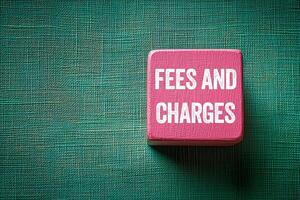 Fees and charges message written on pink wooden cube on green fabric background. Conceptual fees and charges symbol. Copy space. photo