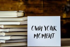 Own your moment message written on white card with stack of books photo