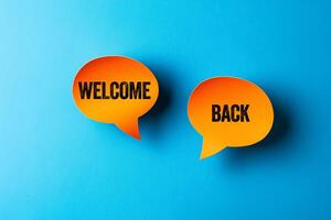Welcome back message written on orange paper speech bubbles on blue background. Conceptual welcome back symbol. Copy space. photo