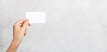 Female hand holding a blank business card, cutaway on gray concrete background with copy space. Branding mockup template photo