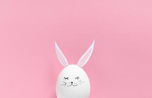 Easter egg with bunny ears and face on pink background with copy space. Flat lay or top view. Minimal concept photo