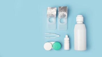Contact lenses set with saline in bottle, tweezers, eye drops, plastic case with solution on blue photo