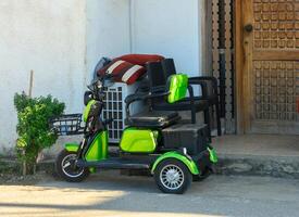 Colorful electric scooter leaning against a rustic door in a sunlit street setting. photo
