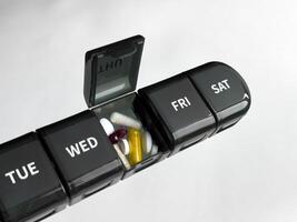 Weekly pill organizer with various capsules and tablets on neutral background photo