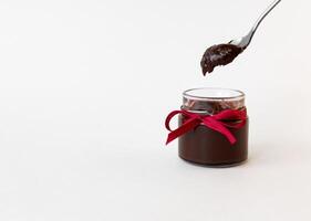 Chocolate spread in jar with red ribbon and spoon on white background photo