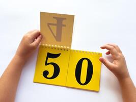 Childs hands flip through yellow pages with numbers. Displaying number 50 on white background photo
