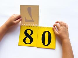 Childs hands flip through yellow pages with numbers. Displaying number 80 on white background photo