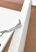 Assembling white furniture with metal wrench and cam lock fastener on brown surface photo