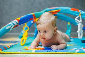 A 2-month-old baby lies on a developmental mat and plays with toys. While playing, the child gets to know the world and learns shapes and colors. Child development photo