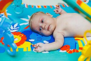 A 2-month-old baby lies on a developmental mat and plays with toys. While playing, the child gets to know the world and learns shapes and colors. Child development photo