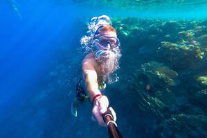 A guy with a mask and snorkel dives into the blue water of the Red Sea and photographs himself photo