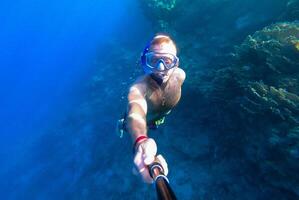 A guy with a mask and snorkel dives into the blue water of the Red Sea and photographs himself photo