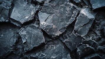 Close up of a rock wall with many different sized rocks. The rocks are all black and appear to be rough and jagged. Scene is one of ruggedness and toughness photo