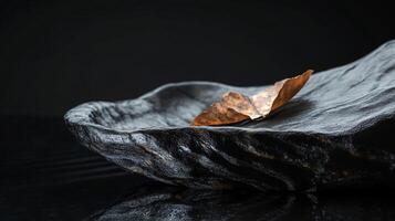Small leaf is floating on the surface of a dark blue stone. The stone is surrounded by water, and the leaf appears to be glowing in the light. Concept of tranquility and peacefulness photo