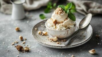 Bowl of ice cream with nuts on top and a spoon next to it. The bowl is on a white plate and the ice cream is in the center photo