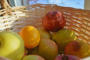 Close up photo sun rays on a wicker basket with apples pomegranates and oranges view from inside the basket. High quality photo