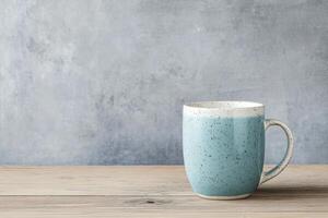 Ceramic mug with blue glaze placed on wooden surface against grey backdrop photo