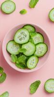 Fresh cucumber slices with mint leaves arranged on a pastel pink background in a bowl photo