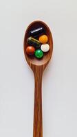 Various colorful tablets and capsules arranged on a wooden spoon against a plain background photo