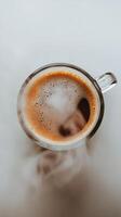 Hot coffee in a clear mug with steam rising on a white table surface photo