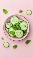 Fresh cucumber slices with mint leaves arranged on a pastel pink background in a bowl photo