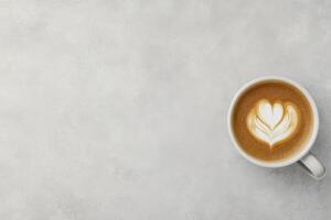 Creamy coffee with heart shaped latte art served in a white cup on a light surface photo